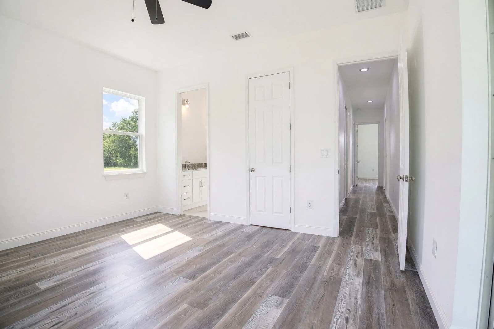 Bright bedroom with a garden-facing window, closet, adjacent bathroom, and hallway