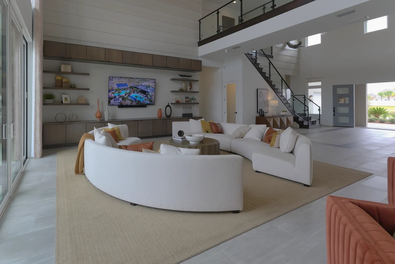 Open-plan living area with a glass-railed loft, floating staircase, and front entry beyond