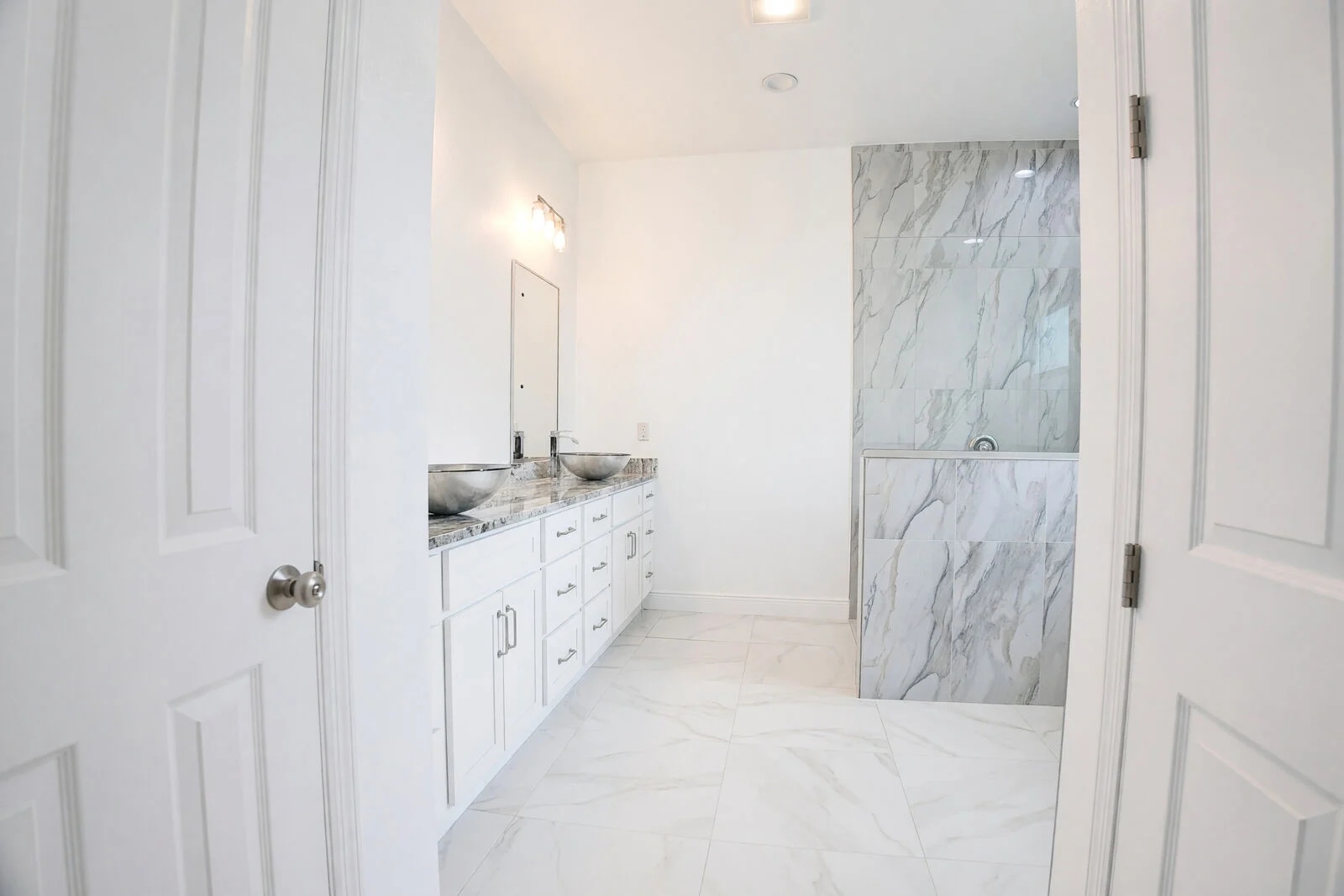 Primary bathroom with a double vanity and marble-look tiled shower